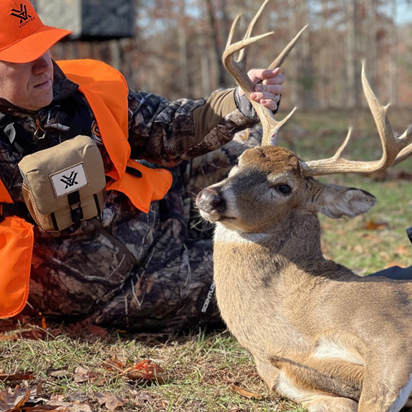 Man posing with his ten-point buck wearing his orange vest for rifle season